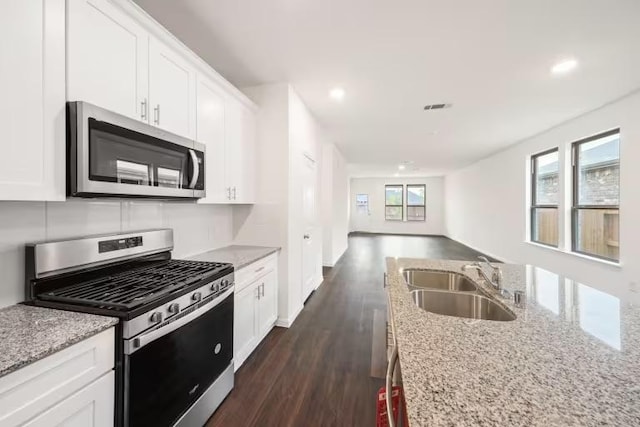 kitchen with stainless steel appliances, a sink, light stone counters, white cabinetry, and recessed lighting