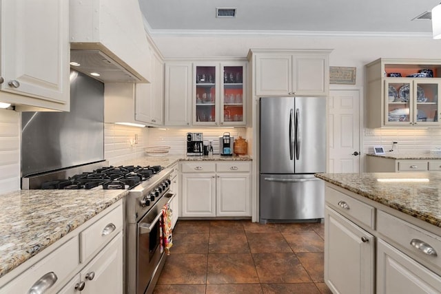 9201 Silver Pine Cv, Austin, TX 78733 - kitchen featuring stainless steel appliances, tasteful backsplash, ornamental molding, custom exhaust hood, and glass insert cabinets