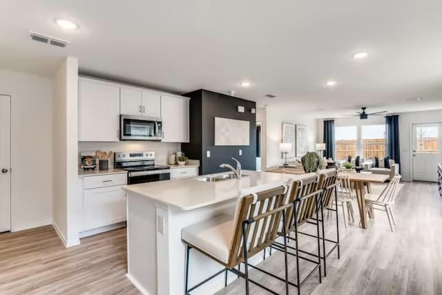kitchen featuring stainless steel appliances, a sink, open floor plan, light wood finished floors, and light countertops