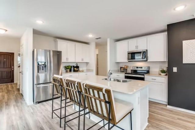 kitchen featuring stainless steel appliances, a sink, light wood-type flooring, light countertops, and a kitchen island with sink