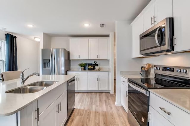 kitchen with appliances with stainless steel finishes, a sink, light countertops, light wood-type flooring, and recessed lighting
