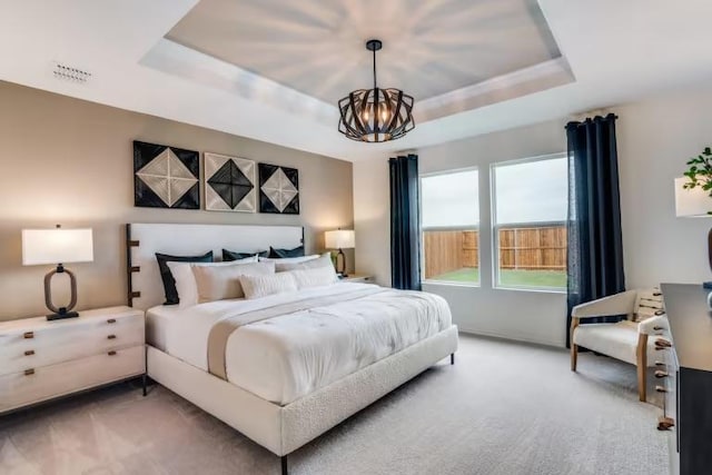 bedroom with a raised ceiling, a chandelier, and light carpet