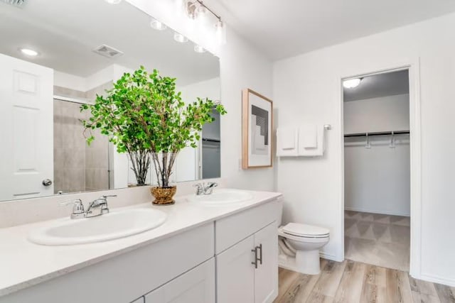 bathroom with a stall shower, toilet, double vanity, a walk in closet, and wood finished floors