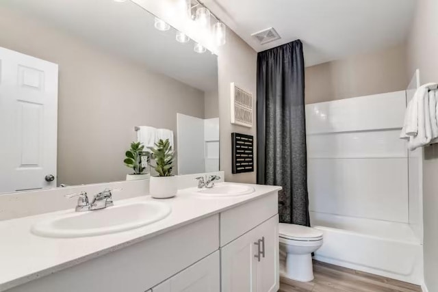 bathroom featuring toilet, wood finished floors, double vanity, and shower / bath combo
