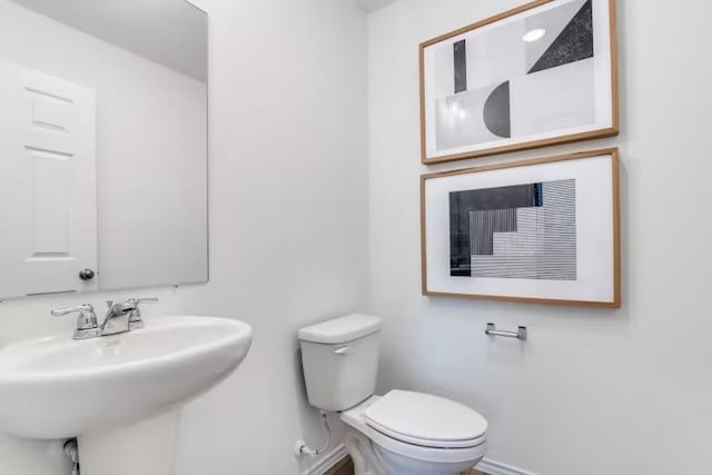 half bathroom featuring baseboards, toilet, and a sink