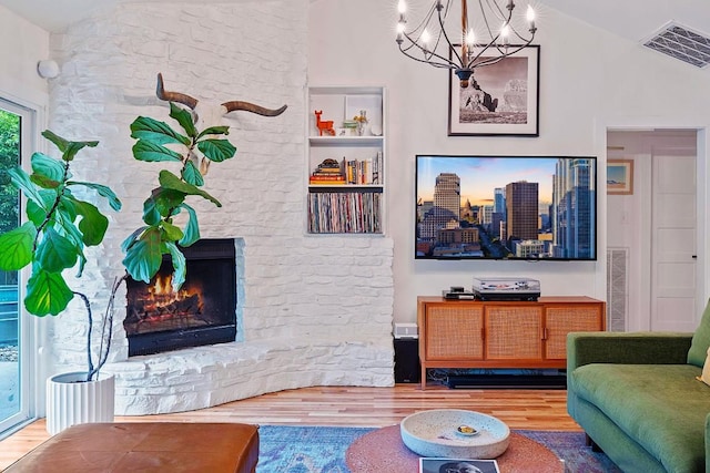 living area with wood finished floors, a chandelier, vaulted ceiling, and a large fireplace