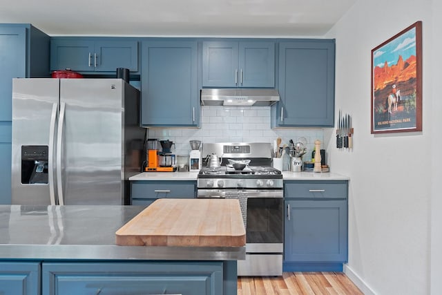 kitchen with appliances with stainless steel finishes, under cabinet range hood, decorative backsplash, light wood-type flooring, and blue cabinetry