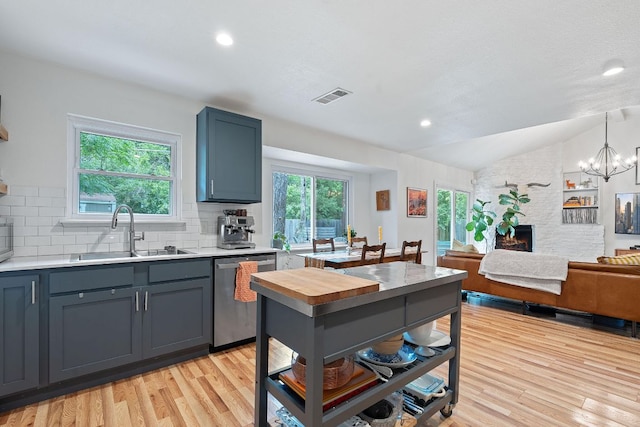 kitchen with stainless steel dishwasher, a sink, lofted ceiling, light wood finished floors, and decorative backsplash