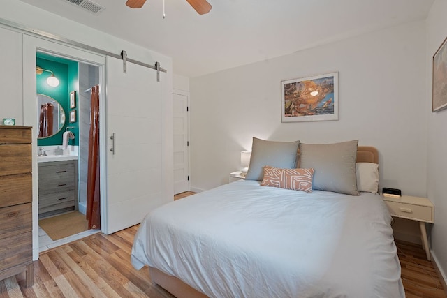 2612 Baxter Dr, Austin, TX 78745 - bedroom featuring a barn door, light wood-style flooring, a ceiling fan, connected bathroom, and baseboards
