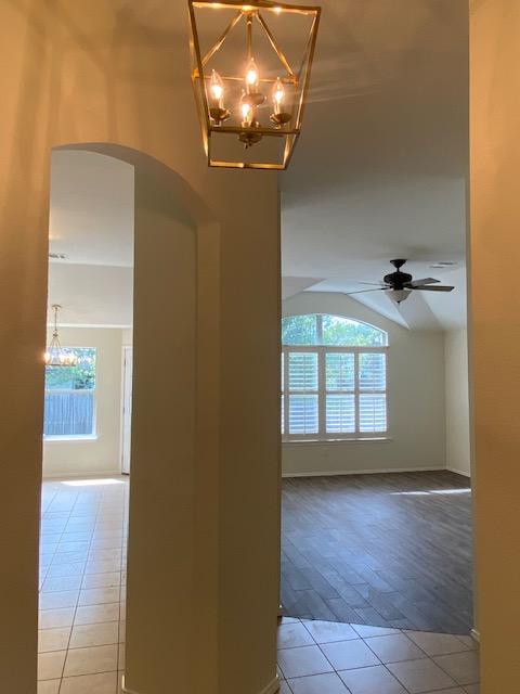 hall with arched walkways, tile patterned floors, healthy amount of natural light, a chandelier, and lofted ceiling