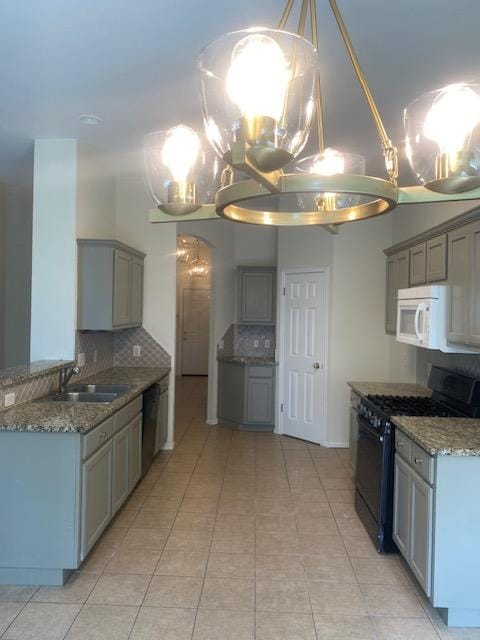 kitchen featuring black range with gas stovetop, a sink, white microwave, tasteful backsplash, and a chandelier