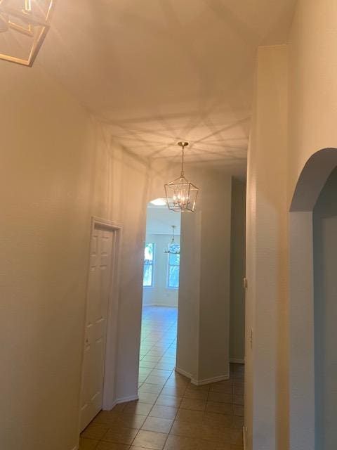 corridor with arched walkways, light tile patterned floors, a chandelier, and baseboards