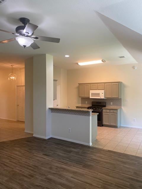 kitchen featuring black gas range oven, white microwave, decorative backsplash, ceiling fan, and baseboards
