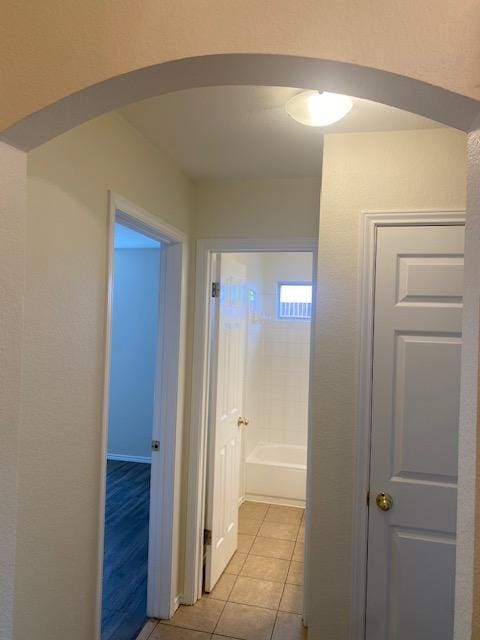 corridor featuring arched walkways and light tile patterned floors