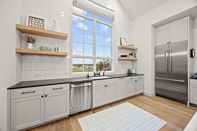 kitchen featuring stainless steel appliances, a sink, open shelves, tasteful backsplash, and dark countertops