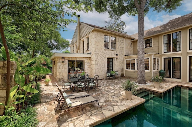 back of property with stone siding, a patio, and an outdoor pool