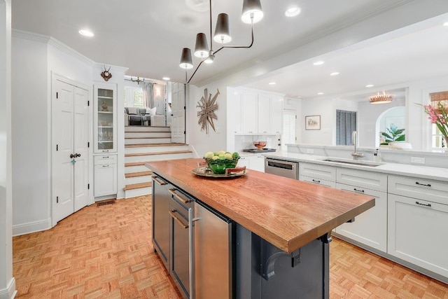 kitchen featuring a sink, butcher block counters, white cabinets, dishwasher, and crown molding
