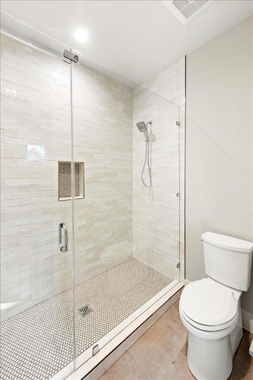bathroom with toilet, a shower stall, and tile patterned flooring