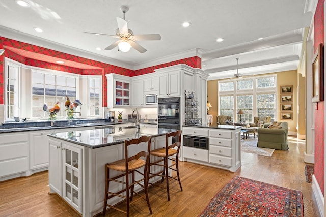124 Florentine, Horseshoe Bay, TX 78657 - kitchen featuring ceiling fan, stainless steel microwave, a kitchen island with sink, white cabinetry, and ornamental molding