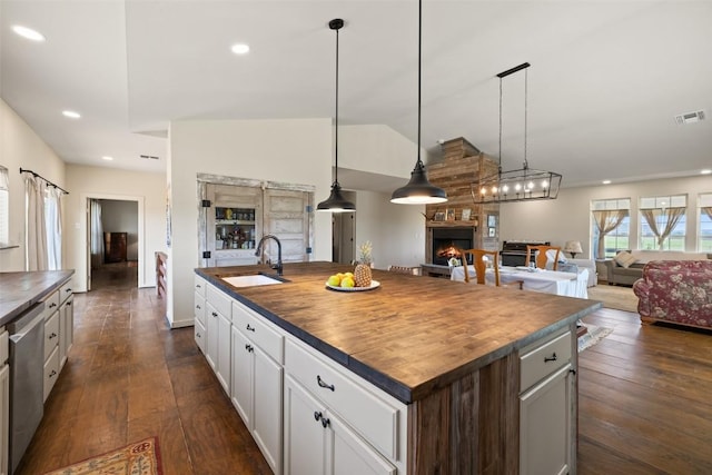 2124 Crabapple Rd, Blanco, TX 78606 - kitchen featuring a sink, butcher block counters, a warm lit fireplace, stainless steel dishwasher, and a center island with sink