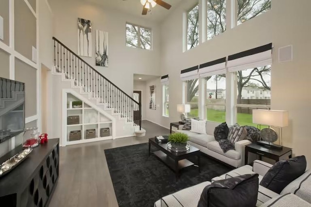 living area with a towering ceiling, stairway, ceiling fan, and wood finished floors
