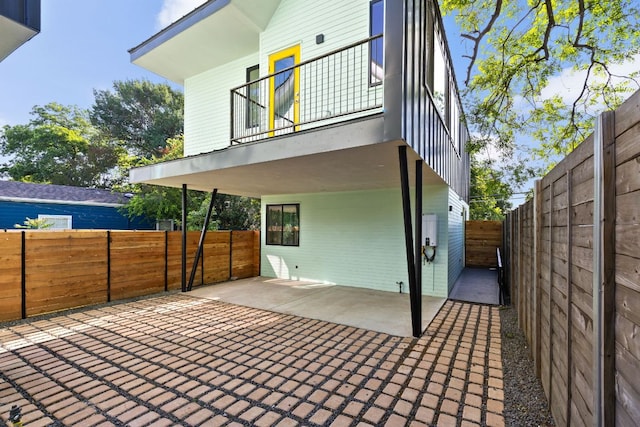 rear view of property with a balcony, a fenced backyard, and a patio area