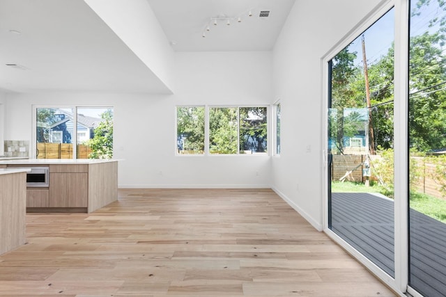 unfurnished dining area featuring rail lighting, light wood finished floors, and baseboards