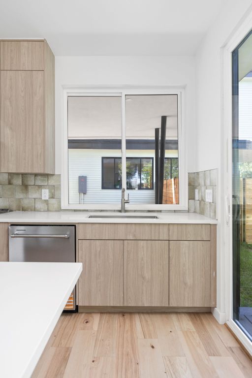 kitchen with light brown cabinetry, a sink, modern cabinets, dishwasher, and light countertops