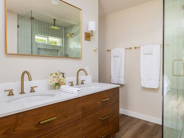 bathroom with a shower stall, double vanity, wood finished floors, and baseboards