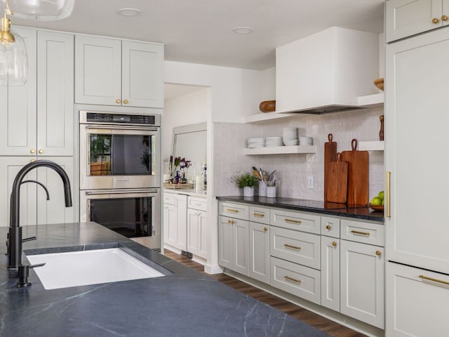 kitchen with double oven, a sink, decorative backsplash, dark countertops, and open shelves