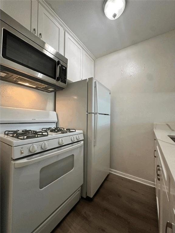 kitchen with white appliances, dark wood-style floors, white cabinetry, and baseboards