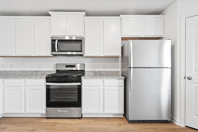 kitchen featuring stainless steel appliances, white cabinetry, light stone countertops, and light wood-style floors