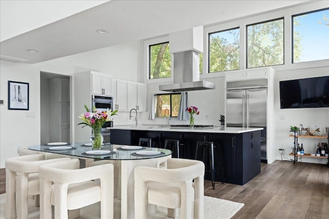 909 Electra, Lakeway, TX 78734 - kitchen featuring wall chimney exhaust hood, stainless steel appliances, light countertops, a towering ceiling, and wood finished floors