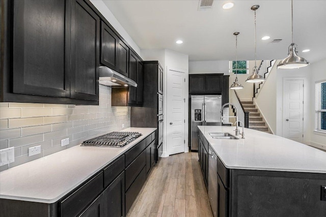 301 Jeffrey David Ln W, Austin, TX 78717 - kitchen with appliances with stainless steel finishes, under cabinet range hood, dark cabinetry, light wood finished floors, and a center island with sink