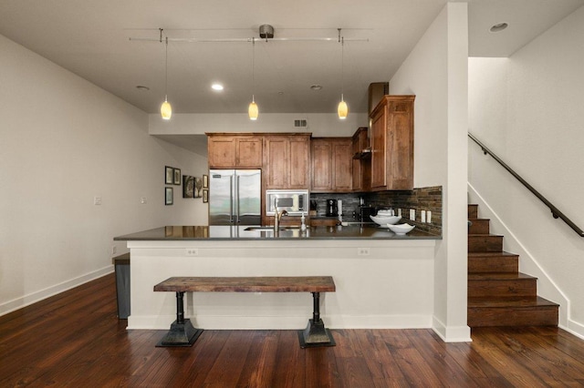 kitchen with built in appliances, dark countertops, a peninsula, brown cabinets, and recessed lighting