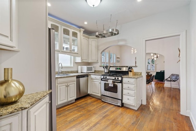 2106 Kenwood Ave, Austin, TX 78704 - kitchen featuring appliances with stainless steel finishes, arched walkways, a sink, light wood-type flooring, and light stone counters