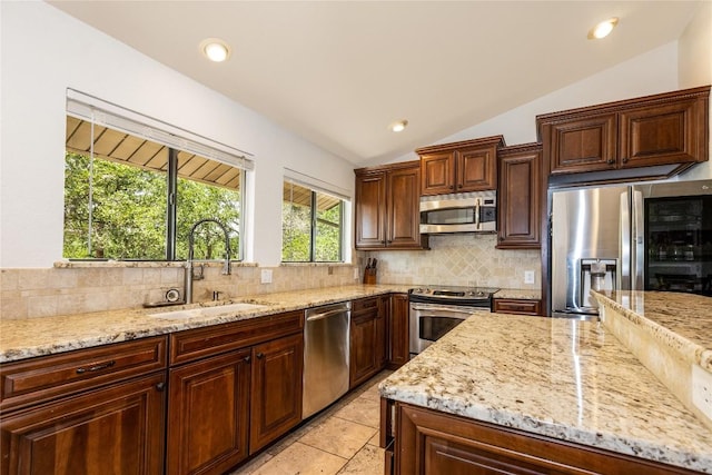 kitchen featuring stainless steel appliances, a sink, decorative backsplash, lofted ceiling, and light stone countertops