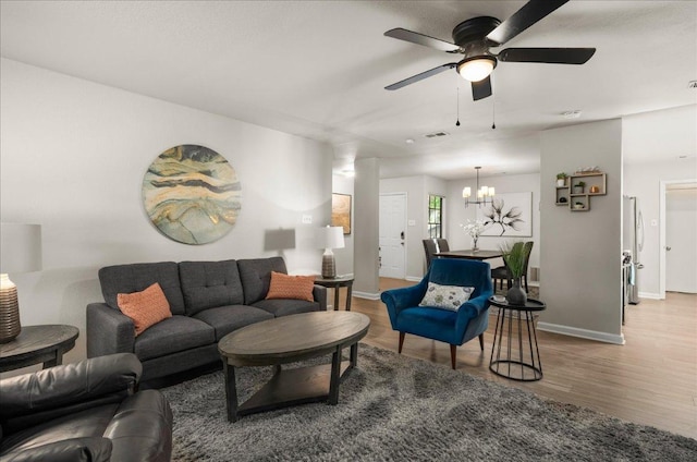 living room featuring wood finished floors, a ceiling fan, baseboards, and a chandelier