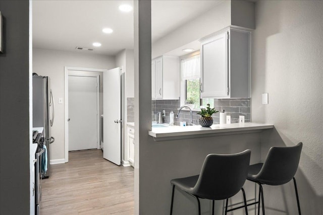 kitchen with a kitchen breakfast bar, light wood-style floors, tasteful backsplash, white cabinets, and light countertops