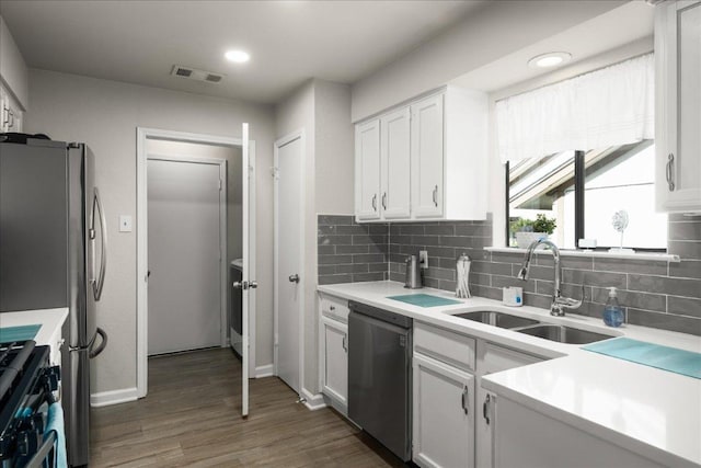 kitchen featuring appliances with stainless steel finishes, a sink, tasteful backsplash, light countertops, and dark wood finished floors