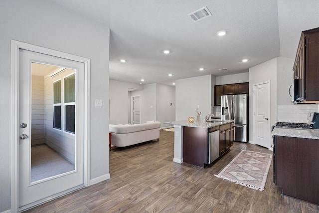 kitchen featuring stainless steel appliances, dark brown cabinets, a kitchen island with sink, dark wood-style flooring, and open floor plan