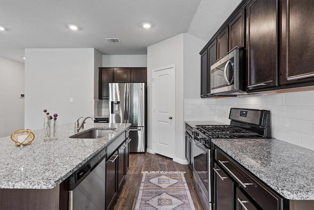 13921 Allan Shivers St, Manor, TX 78653 - kitchen with stainless steel appliances, a sink, dark wood finished floors, light stone countertops, and a kitchen island with sink