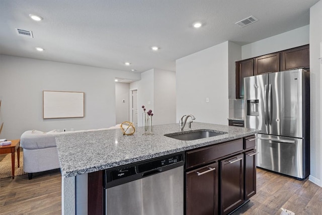 kitchen with appliances with stainless steel finishes, a sink, an island with sink, wood finished floors, and recessed lighting