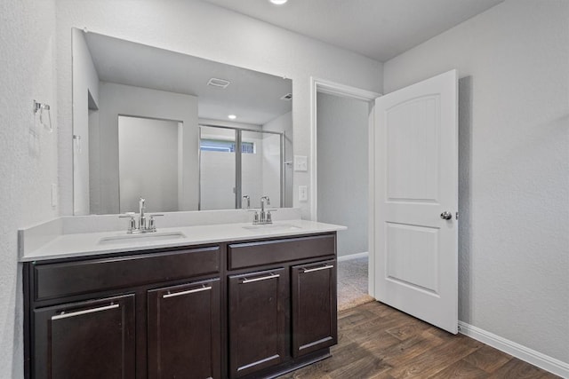 bathroom featuring wood finished floors, a stall shower, double vanity, and baseboards