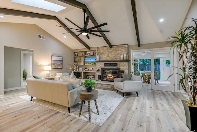 living area with a skylight, high vaulted ceiling, wood finished floors, a stone fireplace, and beamed ceiling