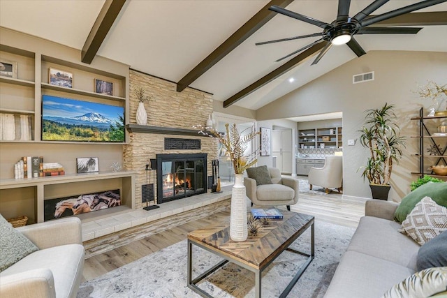 living room with beamed ceiling, a stone fireplace, a ceiling fan, wood finished floors, and high vaulted ceiling