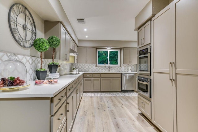 kitchen featuring stainless steel dishwasher, gray cabinetry, light wood finished floors, backsplash, and a sink