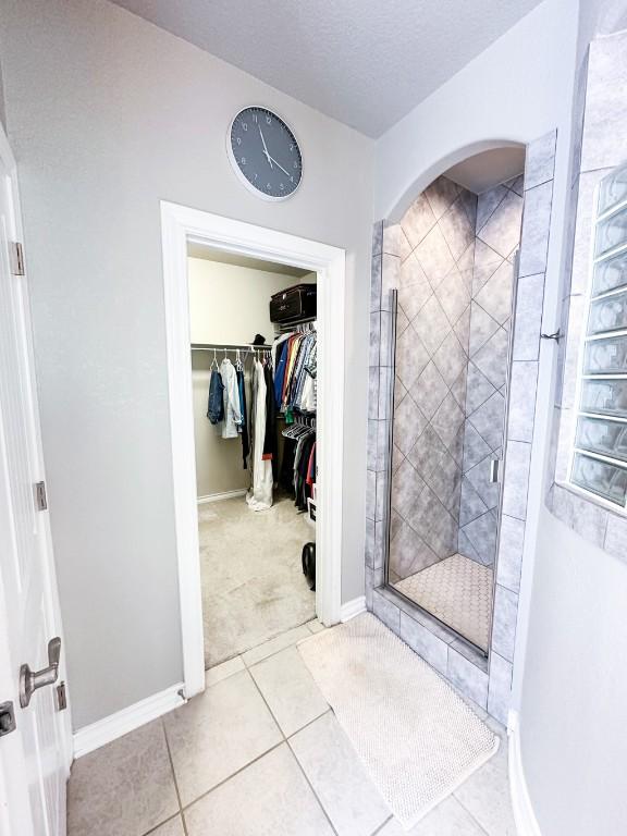 3119 Brand Iron Dr, San Marcos, TX 78666 - bathroom with a stall shower, a walk in closet, tile patterned floors, baseboards, and a textured ceiling