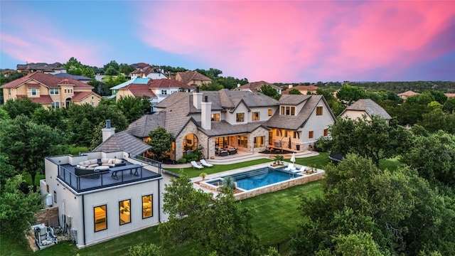 11705 Shoreview Overlook, Austin, TX 78732 - back of house at dusk featuring a chimney, a balcony, a yard, stucco siding, and an outdoor living space