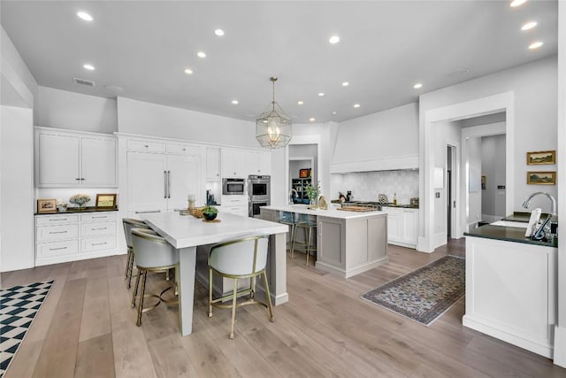 11705 Shoreview Overlook, Austin, TX 78732 - kitchen with a large island with sink, stainless steel double oven, a breakfast bar, light wood-style flooring, and white cabinetry